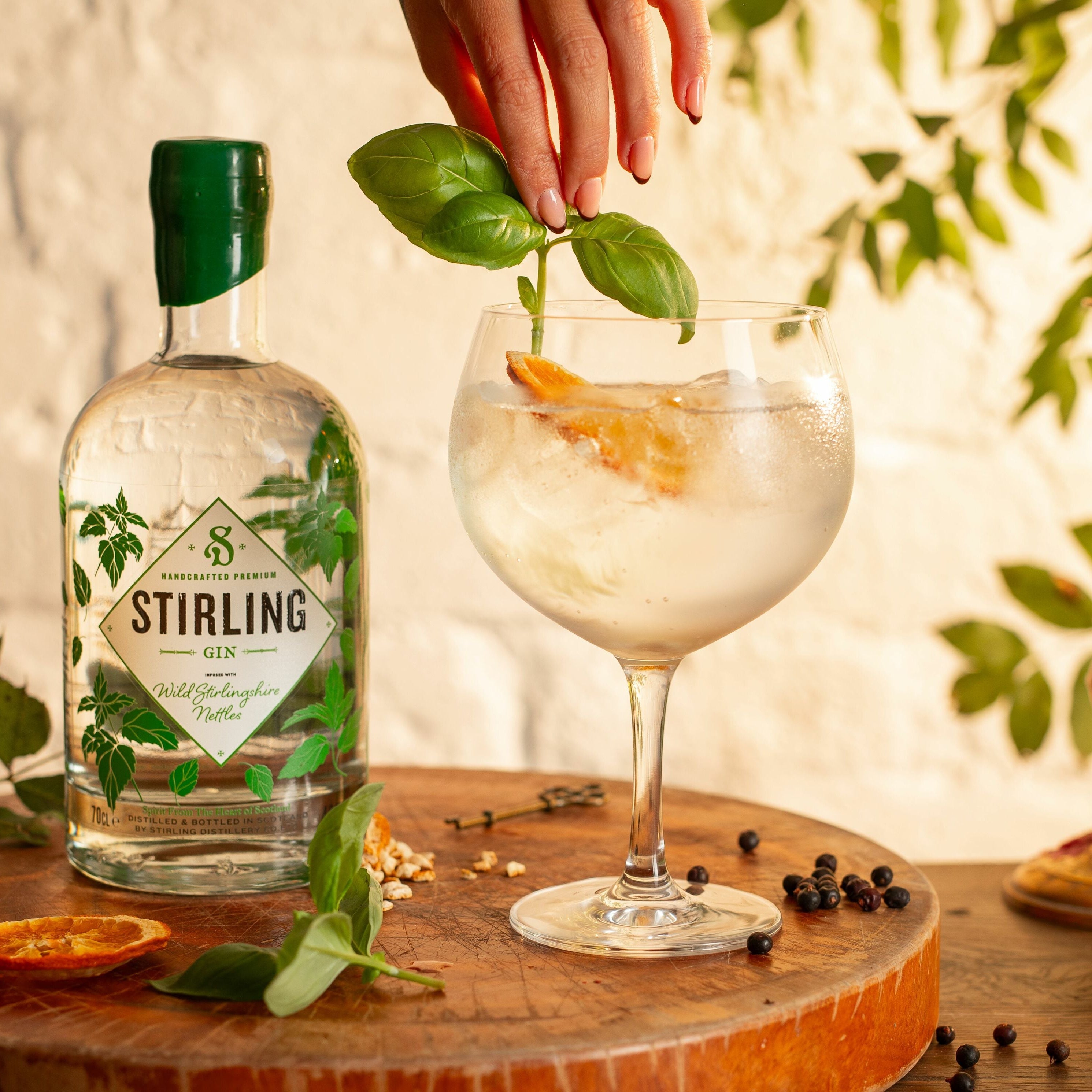 A bottle of Stirling Gin with a green label and wax seal on the lid, decorated with illustrations related to Stirlingshire. A gin and tonic is being served beside it.