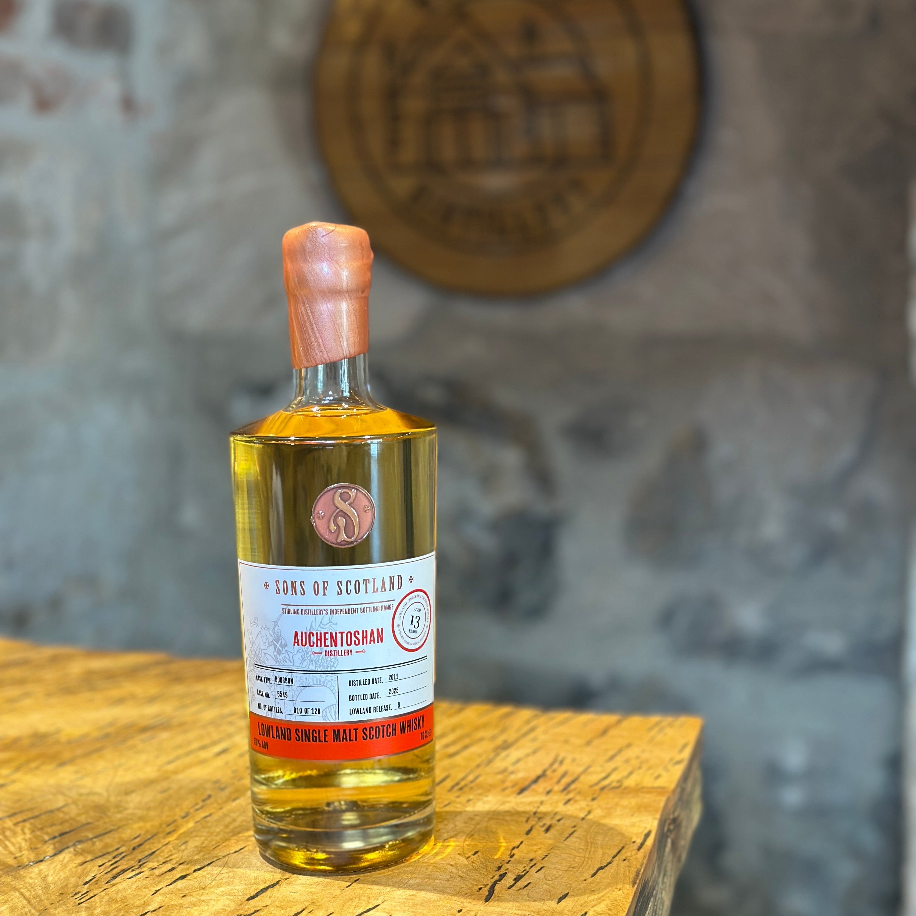 Bottle of Auchentoshan whisky on a wooden table with a blurred stone wall background