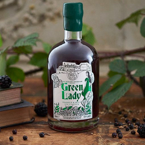 A bottle of green lady liqueur on a wooden surface surrounded by plants and brambles.