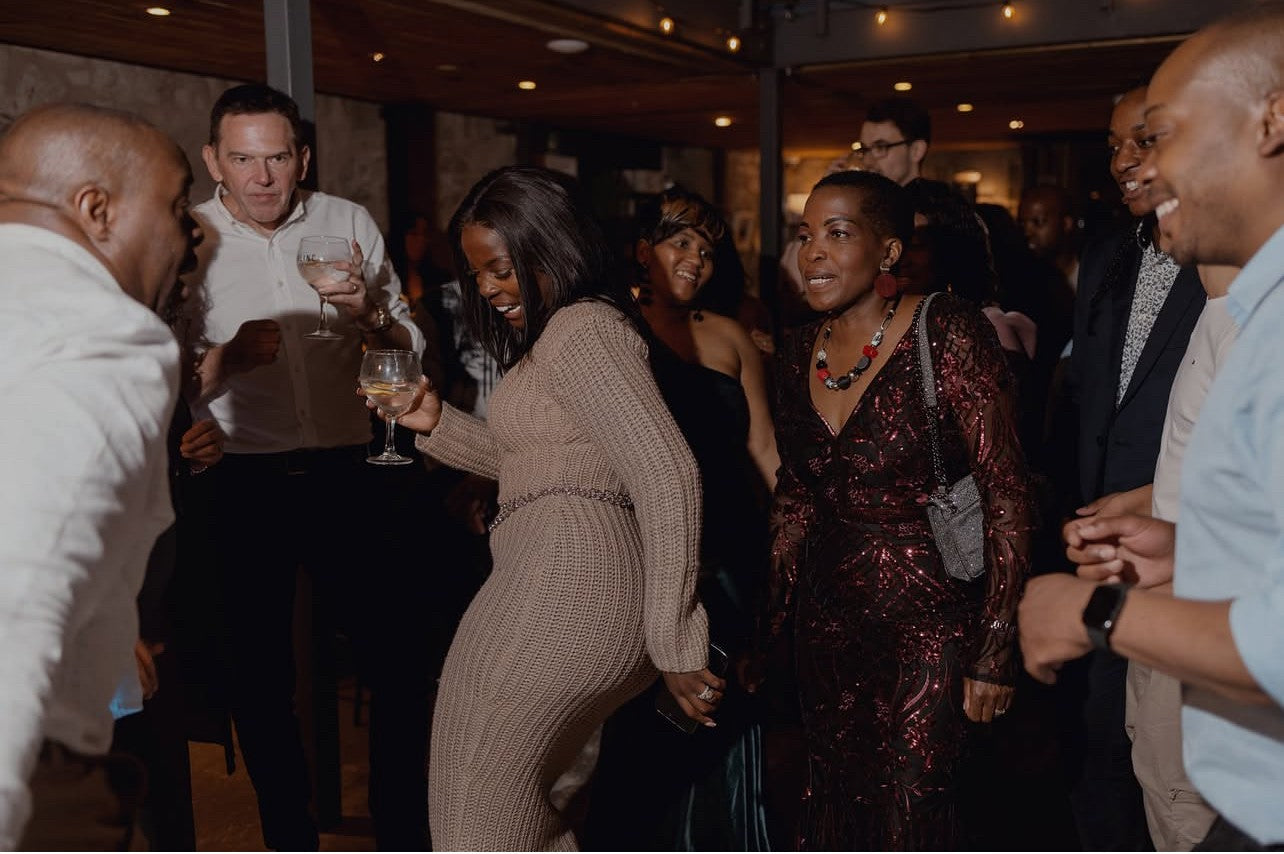 Group of people socializing at a party with drinks in a dimly lit indoor setting.