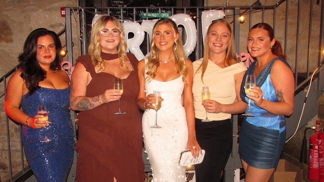 Five women posing together at a party, holding drinks.