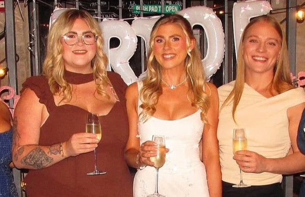Five women posing together at a party, holding drinks.